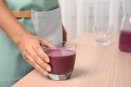 Woman holding glass of delicious acai juice on table, closeup