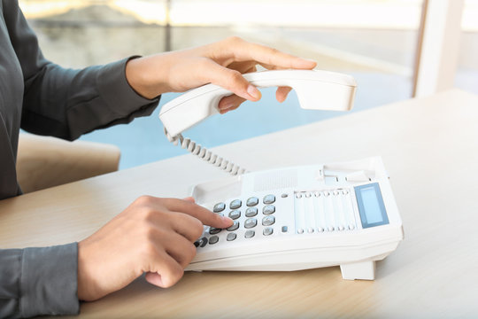 Woman dialing number on telephone at table in office