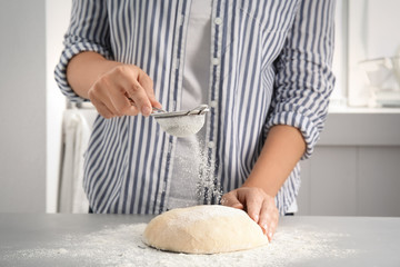 Woman sprinkling dough for pastry with flour on table