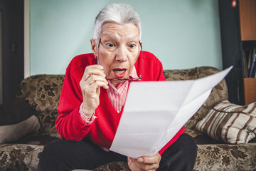 Senior old woman shocked with the bills she receives, appalled and gasping
