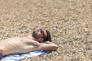 Young man laying on the sandy beach next to a coastline, sunbathing and enjoying vacations