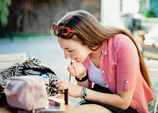Young woman puts some make up on while sitting at garden table in front yard