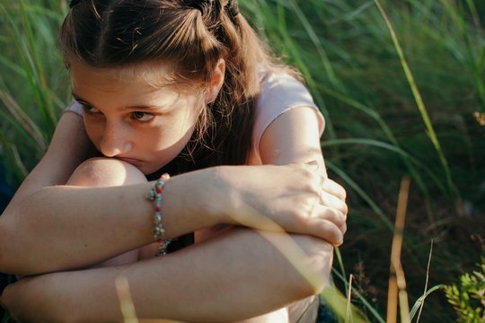 Closeup portrait of upset teenage girl sitting on the grass