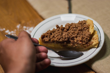 white plate with an apple pie slice  on a wooden background, a vintage spoon and a brown cloth 