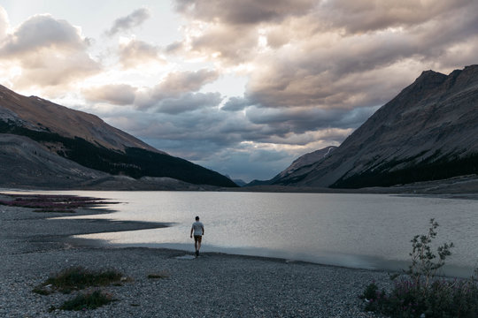 Young male stands next to peaceful lake during sunset in Canadian wilderness