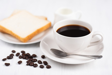 Cup of black coffee with roasted coffee bean and sliced bread on white table, breakfast