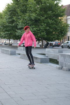 Redhead female teenager rolling with skateboard in the city square