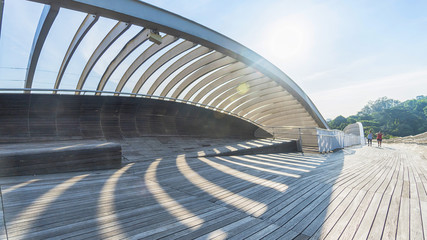 people in wooden bridge walkway with shadow of steel structure from sunlight over forest tree green...