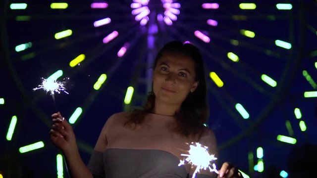 An attractive young girl enjoys a holiday with fireworks in her hands having a good mood. slow motion.