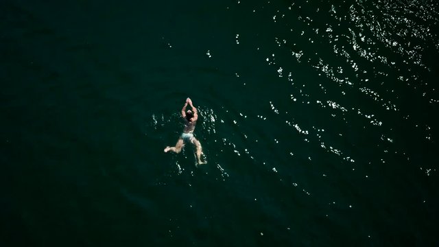 aerial drone footage of a girl swimming in a green lake