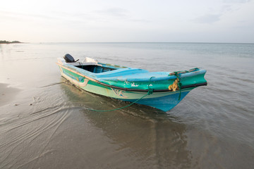 Beached and anchored small fishing boat at sunset on Nilaveli beach in Trincomalee Sri Lanka Asia