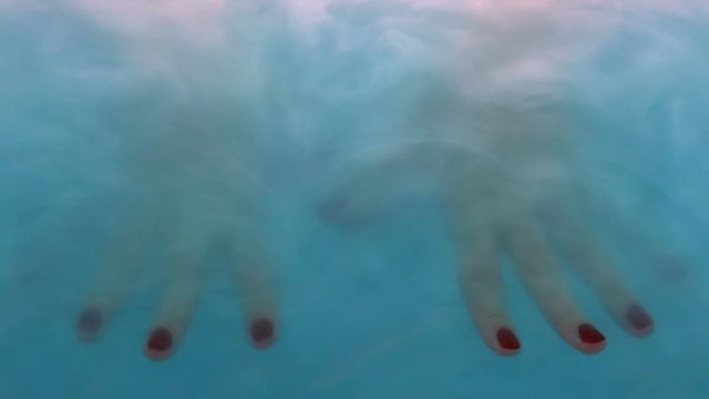 Female hands emerging from blue haze, concept of handcare, soft skin, closeup