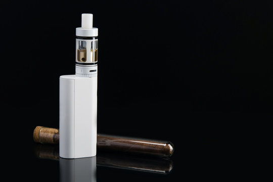 white electronic cigarette on a black background, with a cigar in a glass case next.