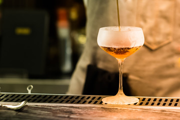 Professional bartender pouring cocktail from shaker into the glass. Mixing alcoholic drink process. Close up image with blurred part of human body on background. Club industry concept. 