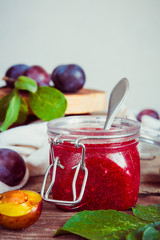 jam from fruit red plum in a glass jar and berries in a bowl on a table with copy space