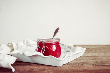 jam from fruit red plum in a glass jar and berries in a bowl on a table with copy space