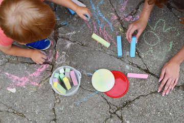 Little boy and his older sister drawing with colorful chalk crayons on old grunge cracked concrete...