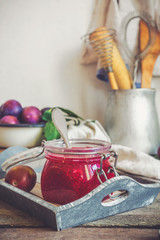 jam from fruit red plum in a glass jar and berries in a bowl on a table in rustic kitchen in vintage style toned with copy space