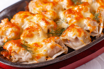 Fried dumplings with onion and bacon on a cast iron frying pan. molten cheese