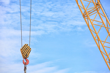 Yellow lifting hook on the cable, with a free place for the inscription on the blue sky.