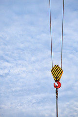 Yellow lifting hook on the cable, with a free place for the inscription on the blue sky.