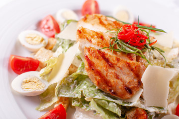 Caesar salad with quail eggs, cherry tomatoes, Parmesan cheese and grilled chicken in white plate on light table.