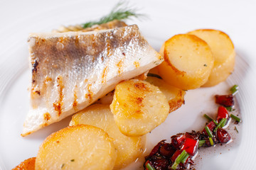Roasted cod, codfish with baked potatoes and vegetables with pickled cucumber and herbs sauce on a white background Restaurant serving. restaurant menu