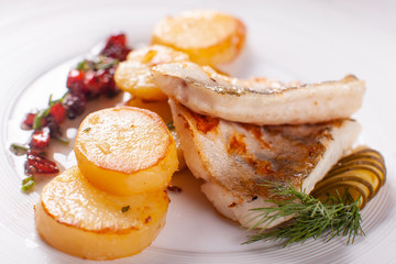 Roasted cod, codfish with baked potatoes and vegetables with pickled cucumber and herbs sauce on a white background Restaurant serving. restaurant menu