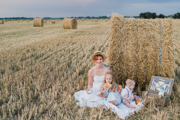 Naklejka na ściany i meble Happy stylish caucasian mother with daughter and son, walking and spending time together in summer wheat field. Mother playing with children outdoors. Love, parenthood, childhood, happiness concept.