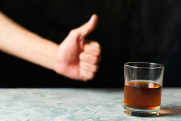 Man hand showing thumb up beside transparent glass with alcohol on gray cement on black background