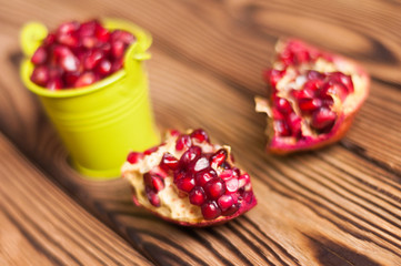 Two halves of fresh ripe red pomegranate with seeds near full green metal bucket of seeds on old brown weathered rustic wooden table