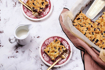 Honeysuckle crumble cake in a baking form and pieces of the cake on vintage plates on cracked concrete background. Homemade streusel berries pie. Breakfast