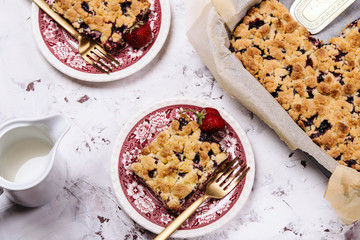Honeysuckle crumble cake in a baking form and pieces of the cake on vintage plates on cracked concrete background. Homemade streusel berries pie. Breakfast