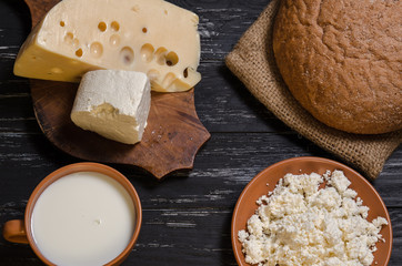 Rural breakfast. Bread, cheese, feta, cottage cheese and milk on a wooden black table.