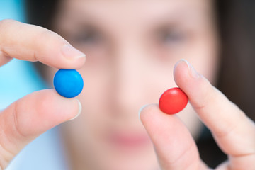 young woman doctor smiling and holding one pill over blue background