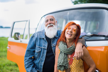 An old hipster couple posing in front of their vintage van 