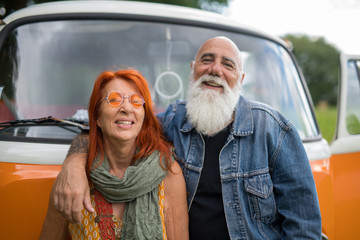 An old hipster couple posing in front of their camper van 