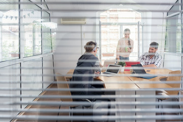 Close-up of the transparent interior window of an office with three young independent workers...