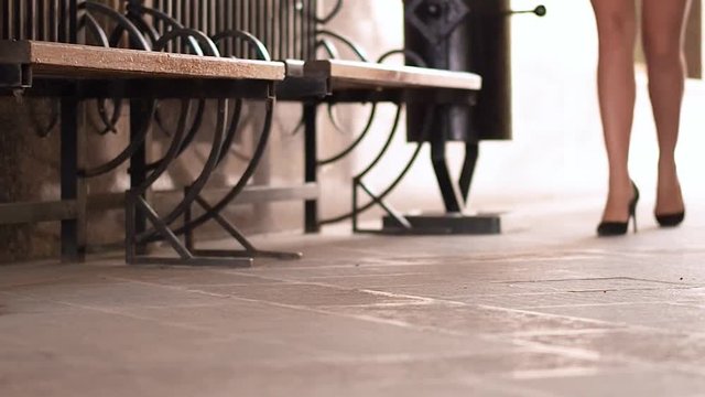 video of elegant young woman stis on the bench and taking off high heel shoes on the street. Feetcare concept.