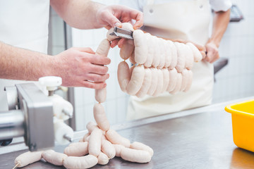 Worker working in butchery producing sausages putting them on beam in a chain