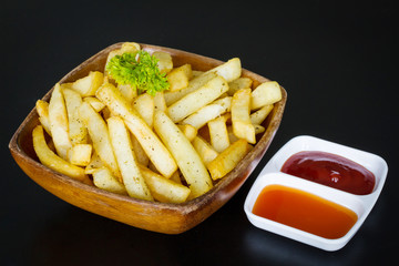French fries in wooden bowl on black background
