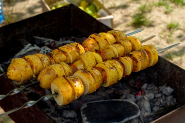 Natural baked potatoes in large pieces with bacon (bacon) on skewers over burning hot coals in the...