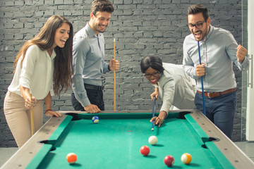 Young cheerful businesspeople playing billiards at office after work. 