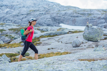 Adventure, travel, tourism, hike and people concept - cheering woman hiker in pink t-shirt walking over mountains nature background. Female admiring views during climbing on Kjeragbolten, Norway.