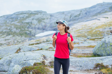 Adventure, travel, tourism, hike and people concept - strong slim woman hiker in pink t-shirt walking over mountains nature background. Female admiring views during climbing on Kjeragbolten, Norway.