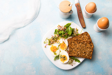 Healthy breakfast: Hard boiled eggs, fresh radish sprouts, arugula and dark whole wheat  bread with herb sauce, on blue background