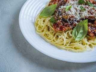 Spaghetti with baked eggplant in a white plate on a gray table.

