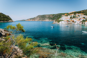 Turquoise transparent lagoon surrounded by green pine trees. Assos village, Kefalonia Greece. Blue deep pattern on Mediterranean sea bottom