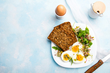 Zdrowe śniadanie: Jajka gotowane na twardo, świeże kiełki, rukola i kromka pełnoziarnistego chleba  na niebieskim tle, miejsce na tekst.  - obrazy, fototapety, plakaty