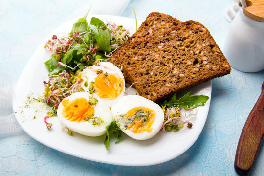 Zdrowe śniadanie: Jajka gotowane na twardo, świeże kiełki, rukola i kromka pełnoziarnistego chleba  na niebieskim tle, miejsce na tekst. 